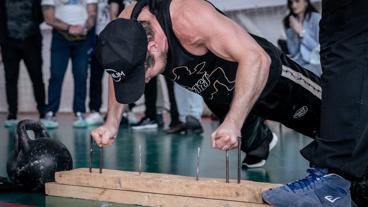A man doing finger push-ups on nails during a gym competition with spectators watching.